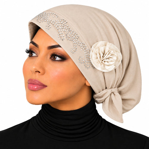 A woman shown in profile wearing a beige hijab with rhinestone embellishments and a cream fabric flower accent, paired with a black turtleneck against a plain white background.