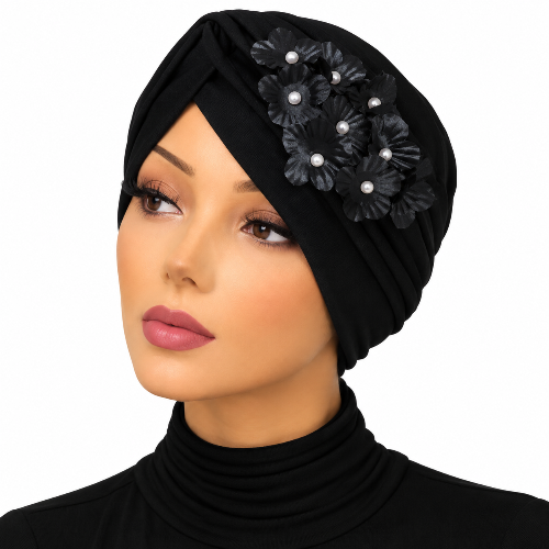 A woman wearing a black turban-style headscarf with decorative black fabric flowers and small pearl-like accents on the side, shown against a plain white background.