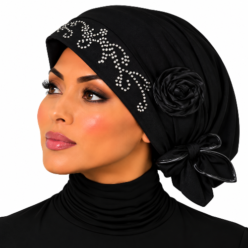 A woman wearing a black hijab with a decorative floral applique, a bow, and a band embellished with small white rhinestones, shown against a plain white background.