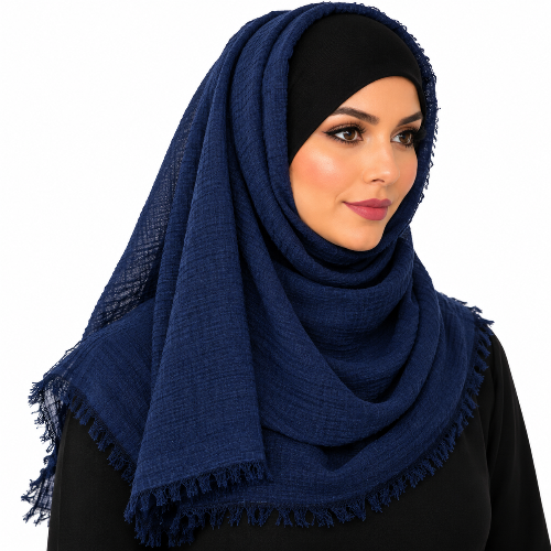 Woman wearing a navy-blue textured hijab scarf with fringe edges, draped around her head and shoulders over a black top against a white background.