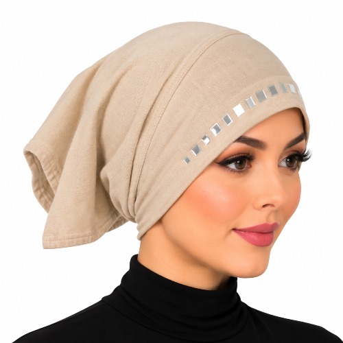 A woman wearing a beige knotted hijab with a row of square silver mirror embellishments along the front edge, shown against a plain white background.