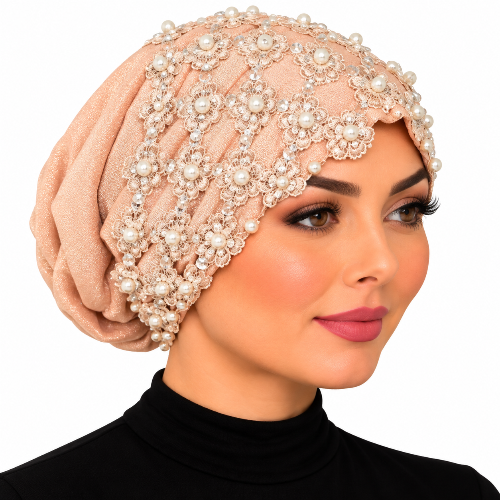 Woman modeling a blush embellished turban with floral lace, pearl beads, and sparkling details on a white background.