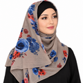 A woman wearing a taupe-beige hijab with a blue and red floral print, styled with a black undercap, against a plain white background.