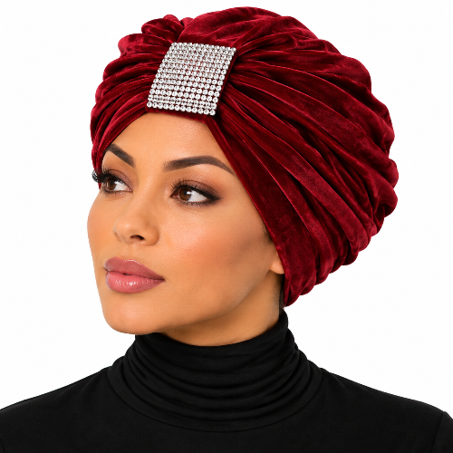 A woman wearing a deep burgundy velvet turban headwrap with a square rhinestone embellishment on the front, paired with a black turtleneck top against a plain white background.