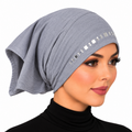 A woman wearing a light gray fabric headscarf or hijab with a row of small square metallic embellishments near the front, shown against a plain white background.