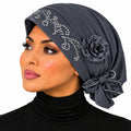 A woman wearing a dark gray hijab with silver rhinestone embellishments and a large fabric flower accent, shown against a plain white background.