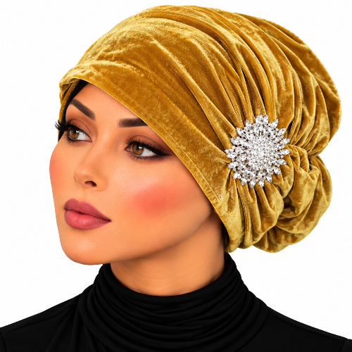 A woman wearing a ruched mustard yellow velvet turban headwrap with a large silver rhinestone brooch, shown in a close-up portrait against a white background.