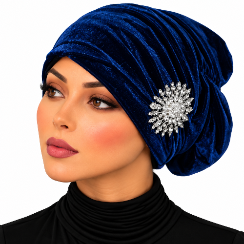 A woman wearing a deep blue velvet slouchy turban hat with a sparkling silver crystal brooch, set against a plain white background.