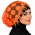 Orange pearl lace hijab cap with floral lace, pearl embellishments, and decorative beaded trim worn by a model on a white background.