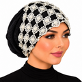 Woman modeling a black embellished turban with white floral lace and pearl bead details on a white background.