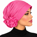 A woman in profile wearing a bright pink turban-style headscarf with a large fabric flower accent on the side, against a plain white background.