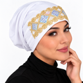 White underscarf cap with ornate gold and iridescent embellished front design modeled by a woman against a clean white background.