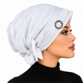 Woman wearing a white pre-tied turban cap with a round rhinestone ring detail